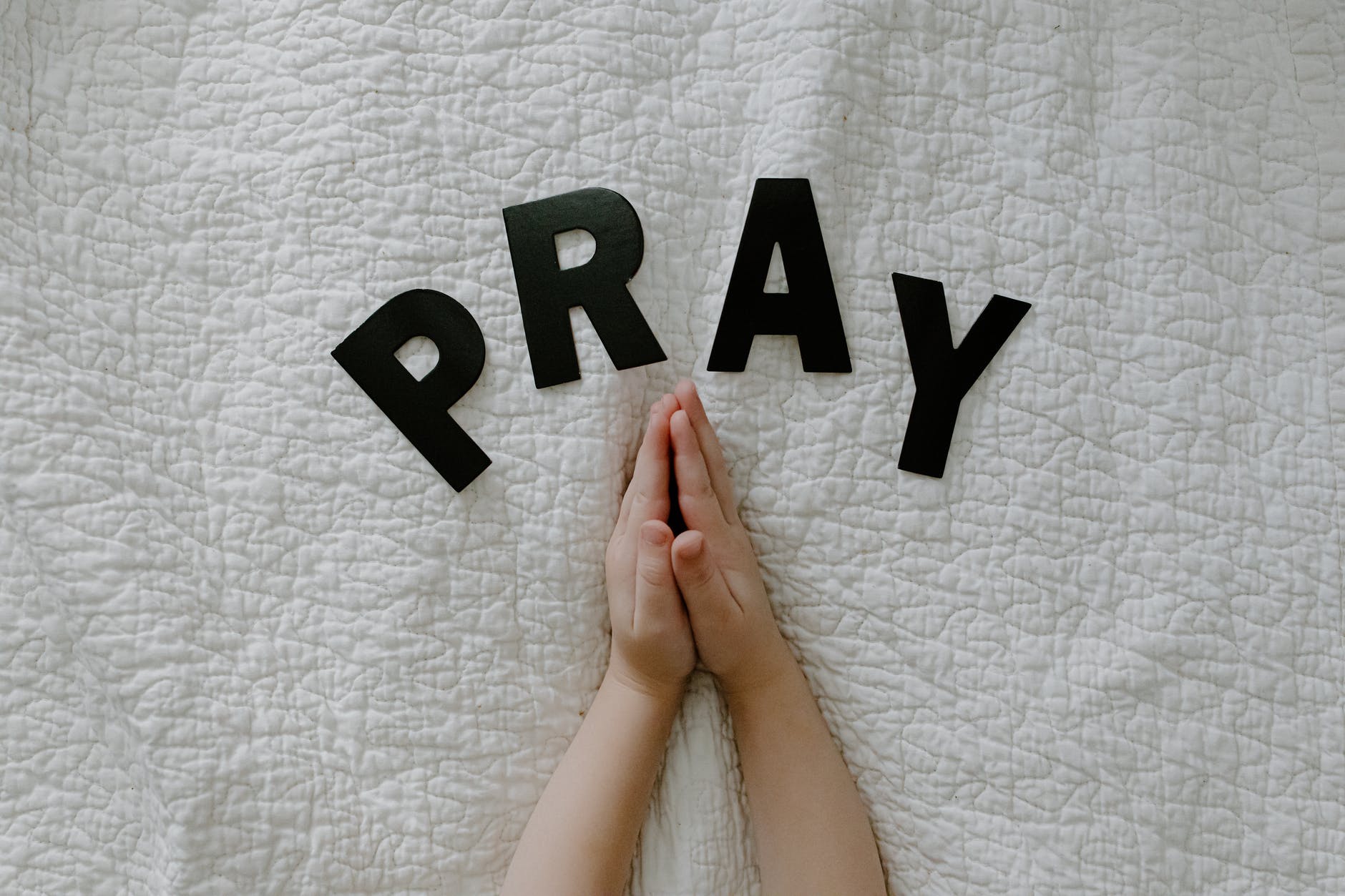 praying hands of a person on white textile