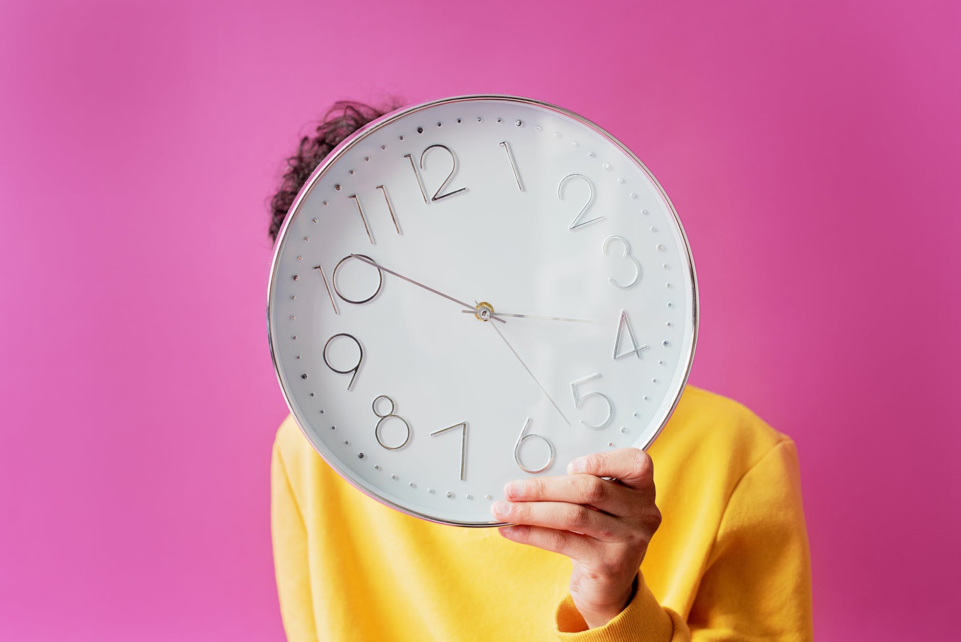 person holding an analog wall clock with purple background